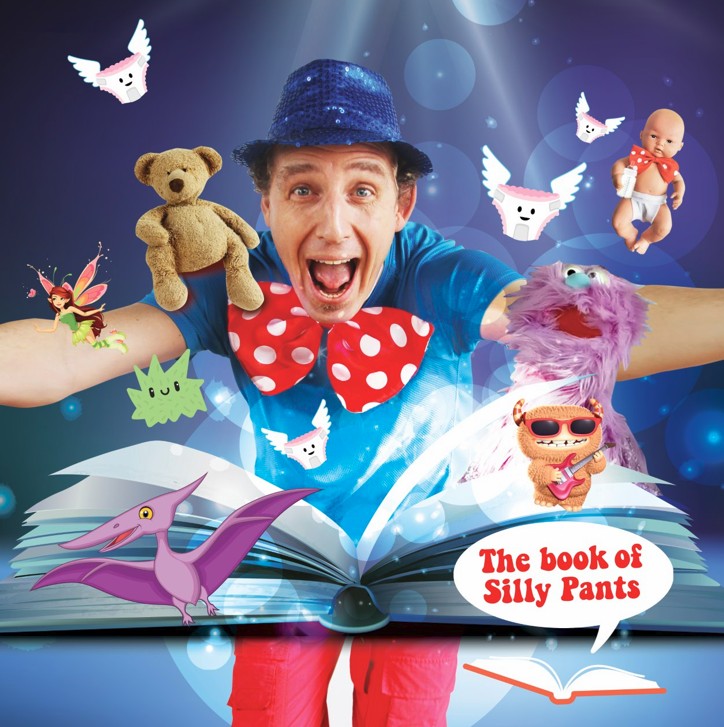 A smiling performer in a blue hat and oversized red polka-dot bow tie pops out of an open book, surrounded by playful characters including a teddy bear, puppet, fairy, flying underpants, dinosaur and guitar-playing cat. A speech bubble reads The Book of Silly Pants