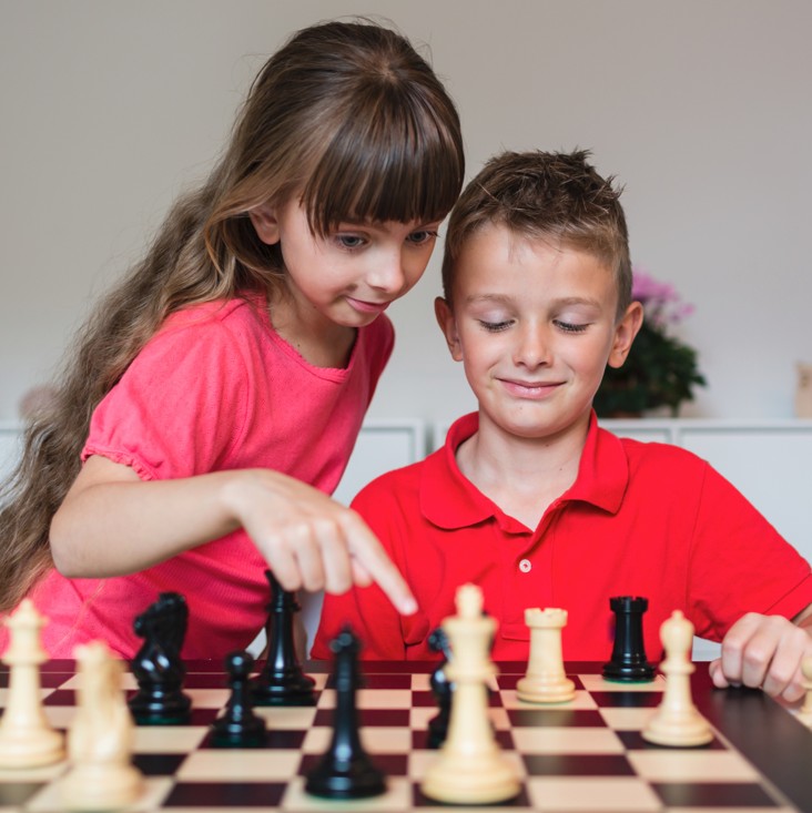 Two children standing behind a chess board