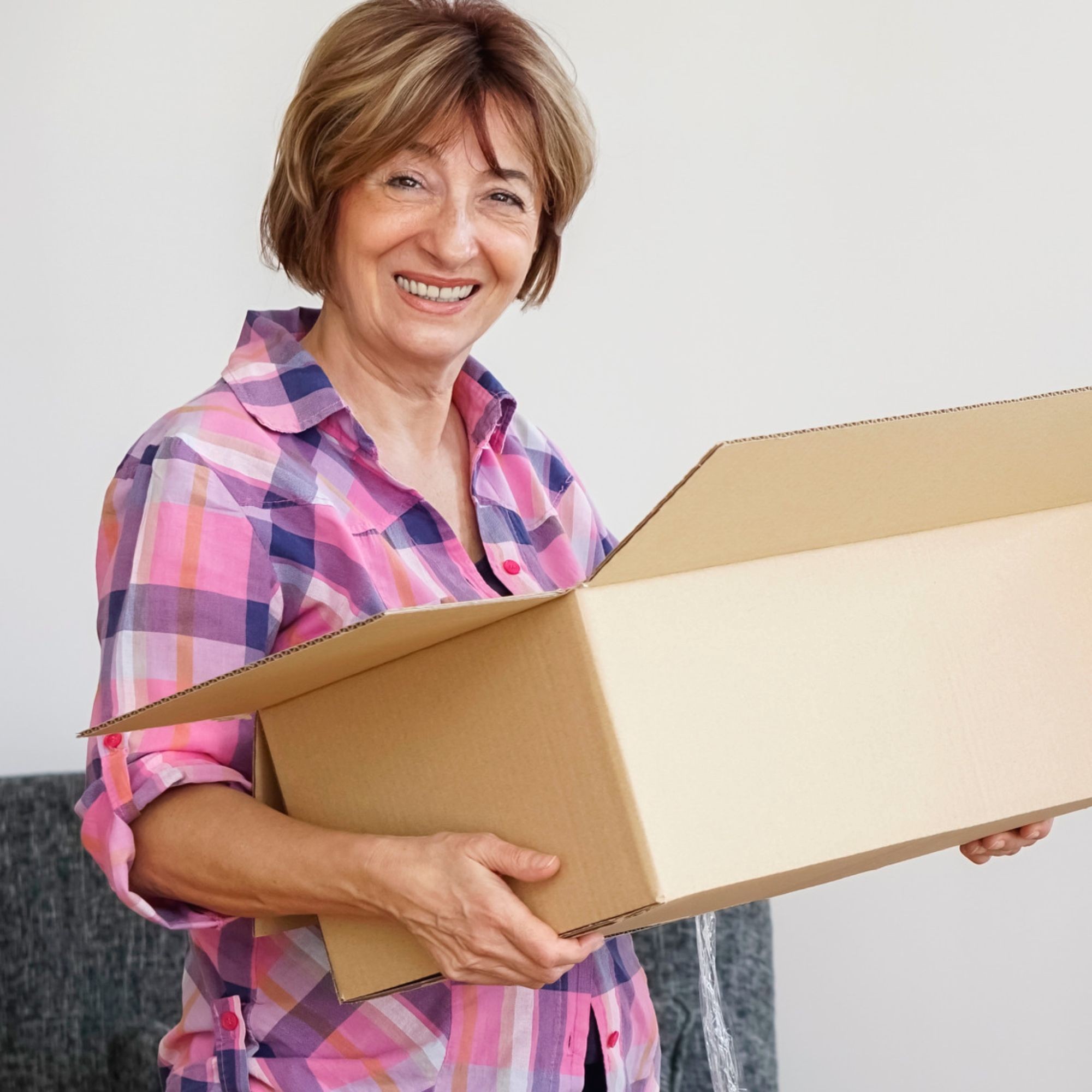 Lady in a flanelette shirt looking at camera smiling and holding a moving box
