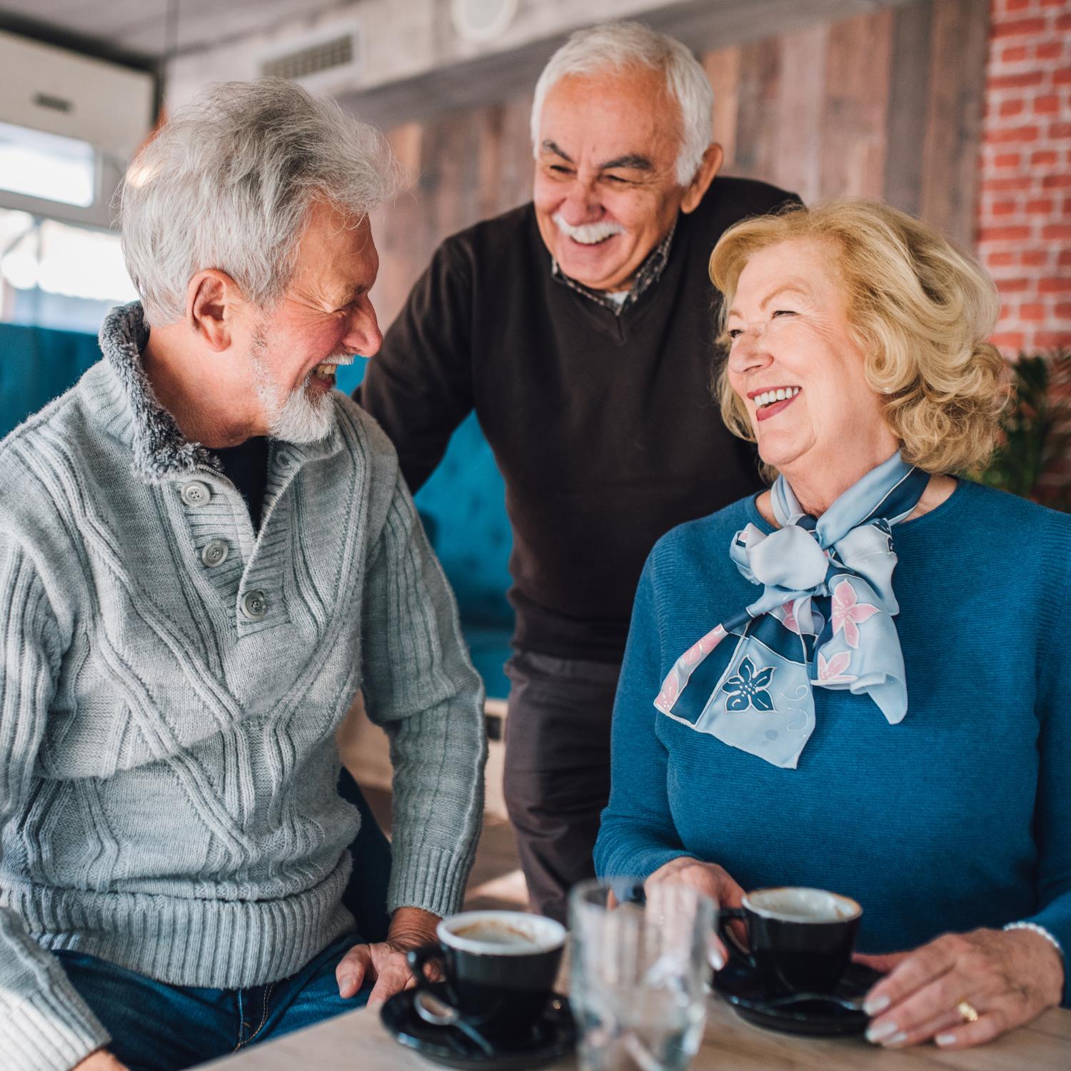 Three older adults laughing together at a cafe