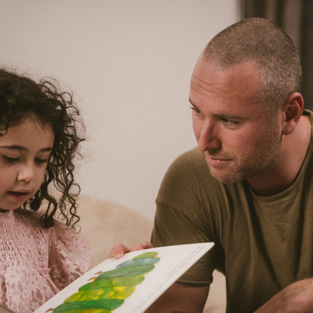 Image of a dad or father figure cuddling a small child. Both are happy and smiling.