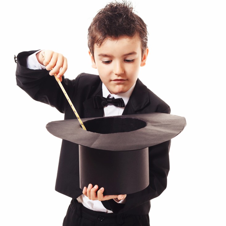 a child dressed as a magician points a wand into a large black hat